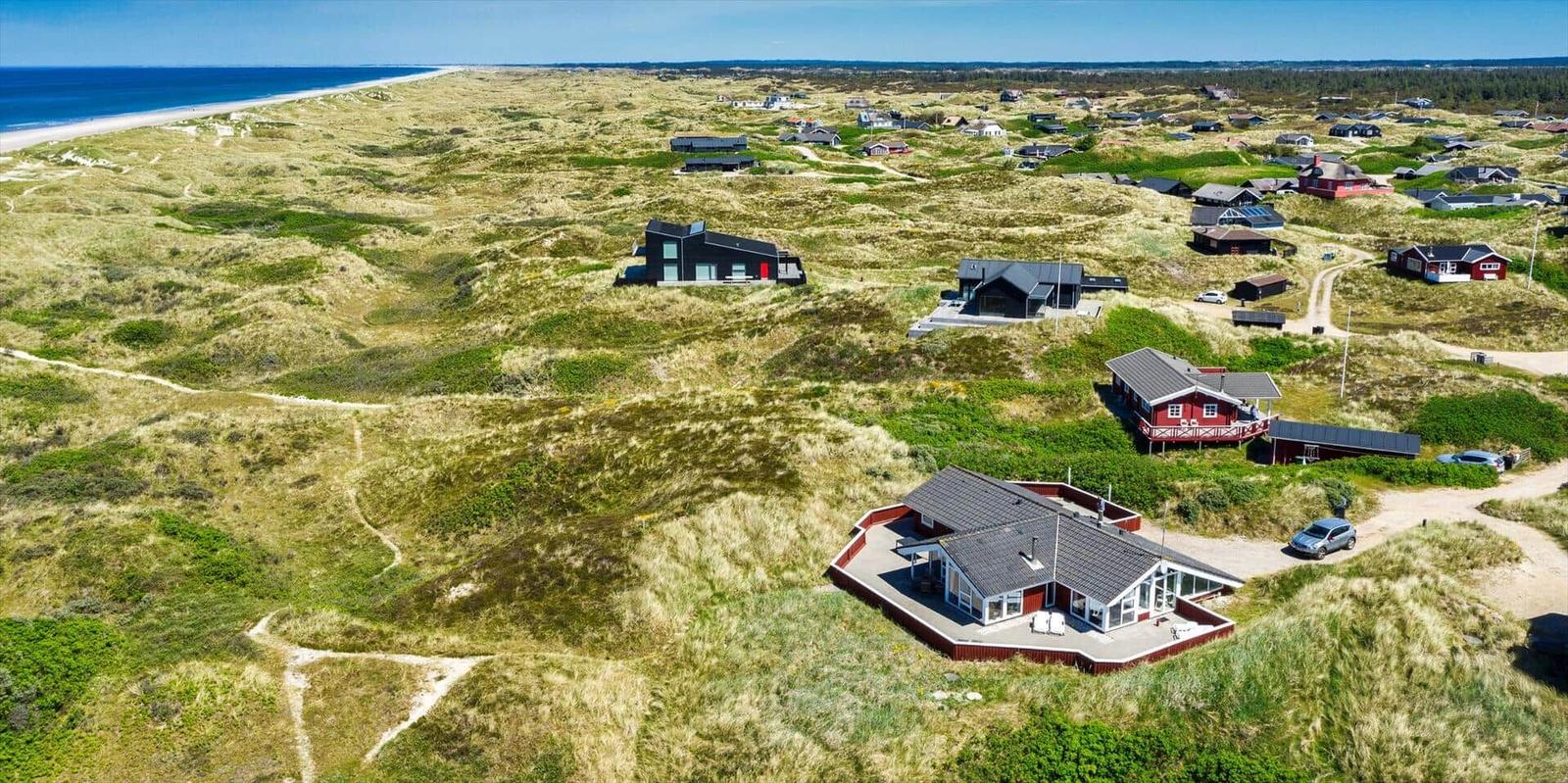 Dorf auf Dünen mit Häusern und Strand im Hintergrund.