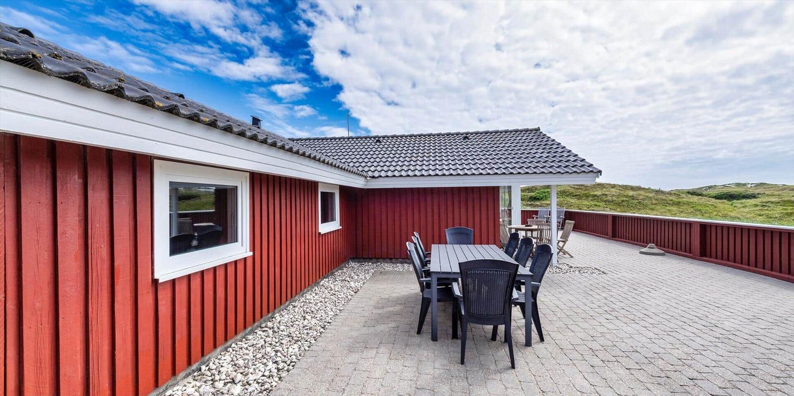 Rotes Holzhaus mit Terrasse und Gartenmöbeln unter blauem Himmel.