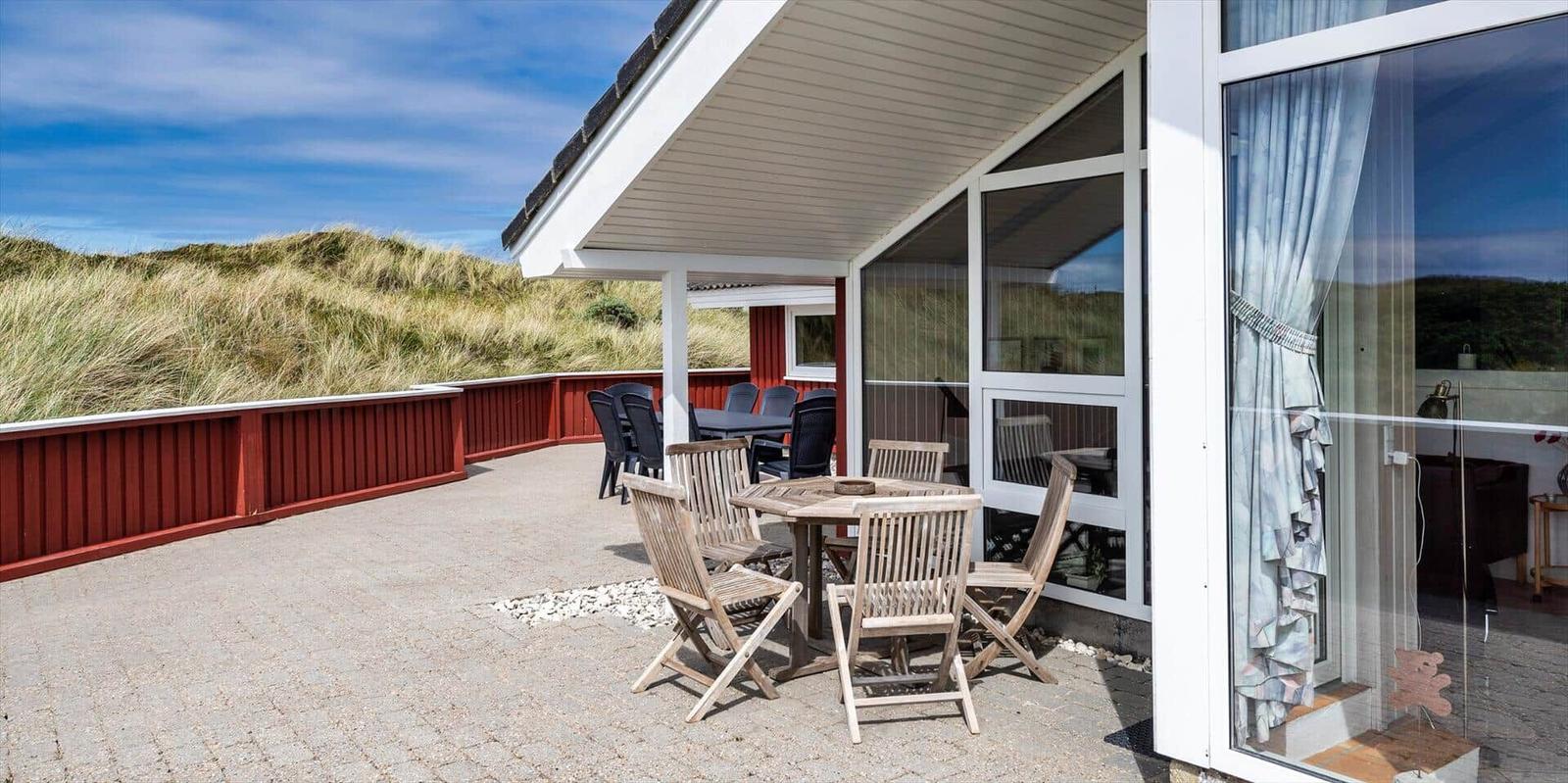 Terrasse mit Tisch und Stühlen neben einem Haus mit Glasfront.
