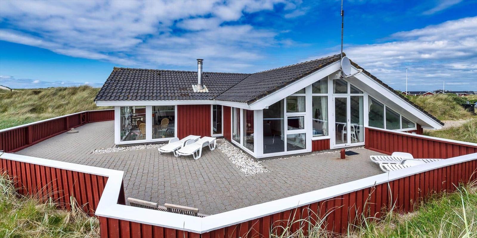 Rotes Ferienhaus mit großem Terrassenbereich und Sicht auf Dünen.