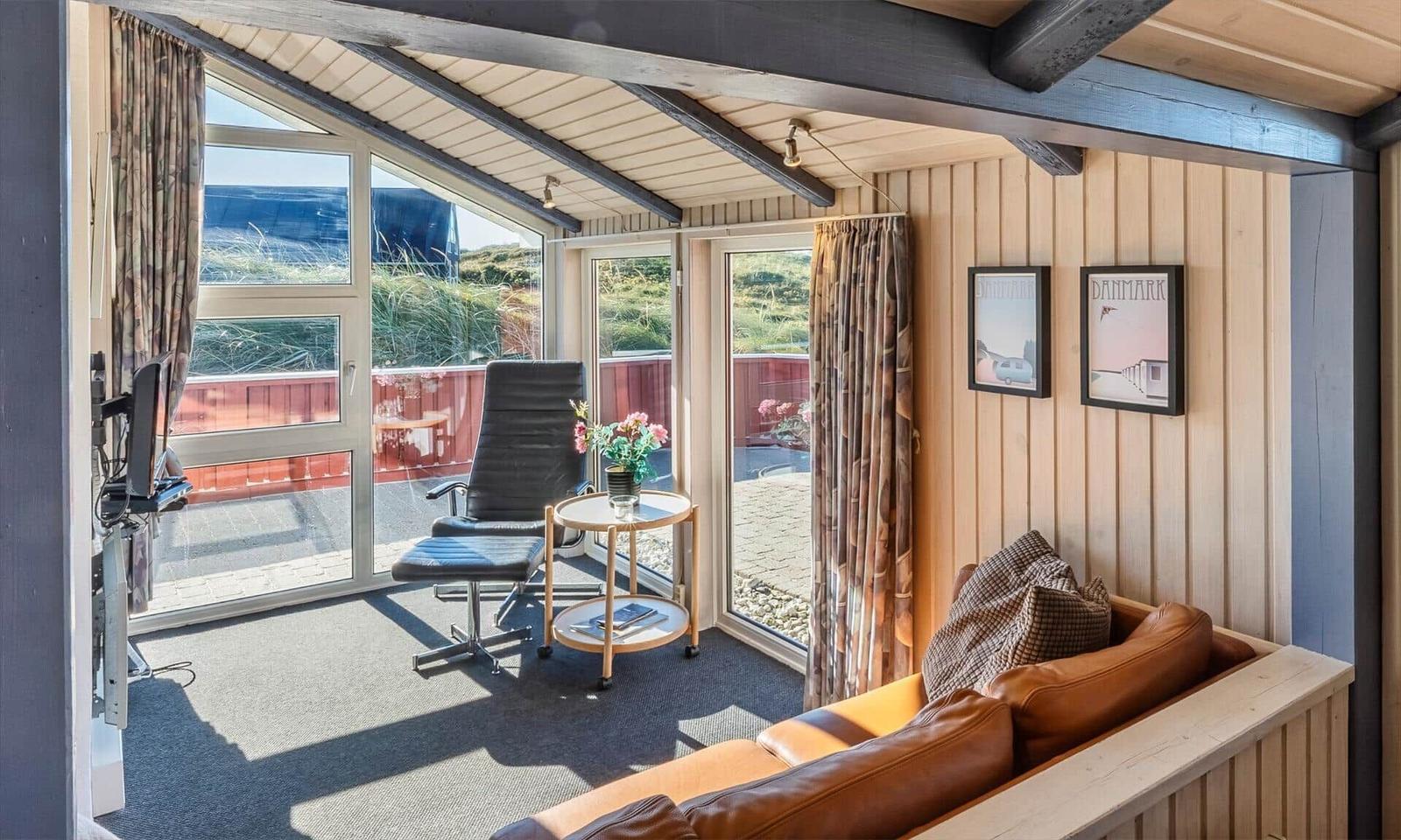 Wohnbereich mit Ledersofa, Sessel und Blick auf den Außenbereich.