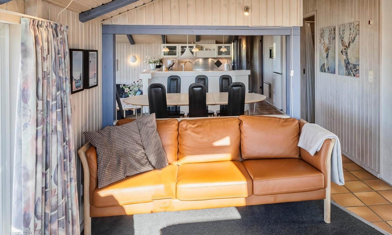 Ein braunes Ledersofa mit Kissen und Decke. Im Hintergrund ist die Küche mit Esstisch und Stühlen sichtbar.