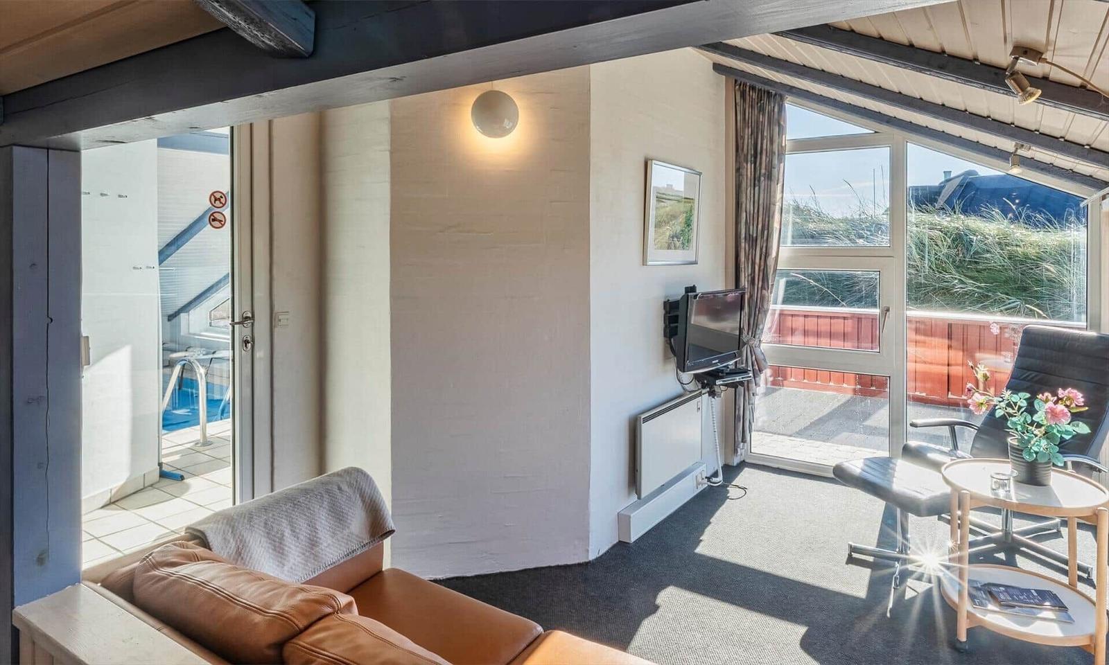 Wohnzimmer mit Sofa, Fernseher und Blick auf Balkon und Pool.