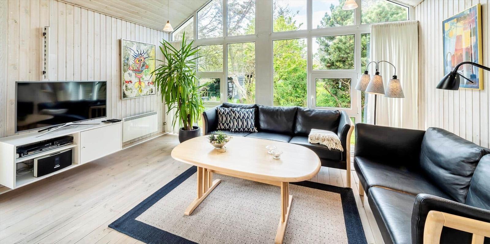 Wohnzimmer mit schwarzen Sofas, Holztisch und großem Fenster zur Aussicht.