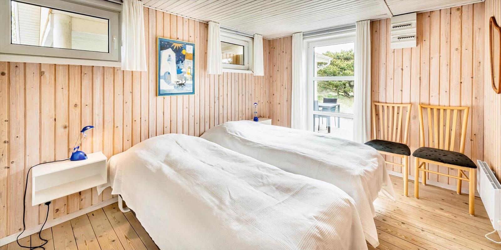 Zwei Betten, Holzwände, Fenster und Stühle im Schlafzimmer.