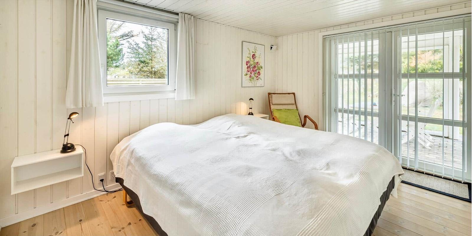 Schlafzimmer mit Bett, Fenster und Glastür zum Balkon.