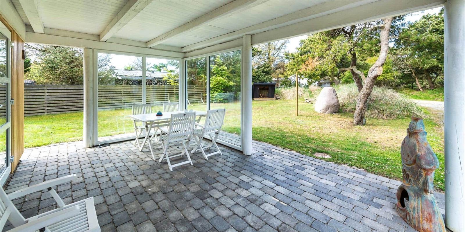 Terrasse mit Tisch und Stühlen, Blick auf Garten und Baum.