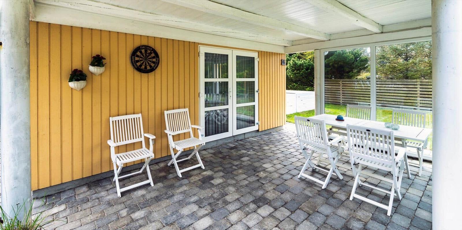 Terrasse mit weißem Tisch und Stühlen, gelbem Holzhaus und Dartscheibe.