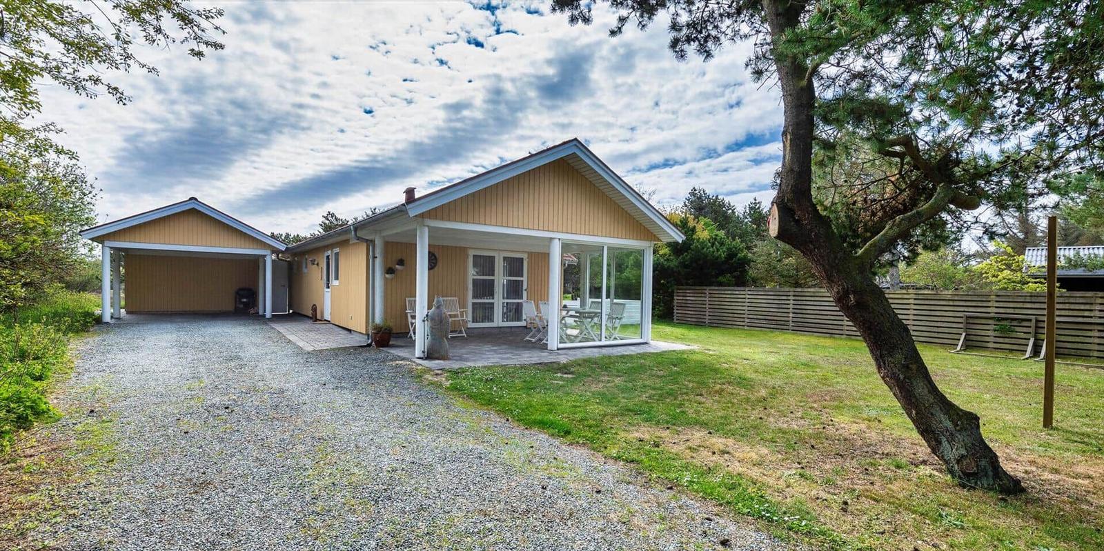 Ein gelbes Haus mit Terrasse und Garage. Grasfläche und Bäume umgeben das Grundstück.