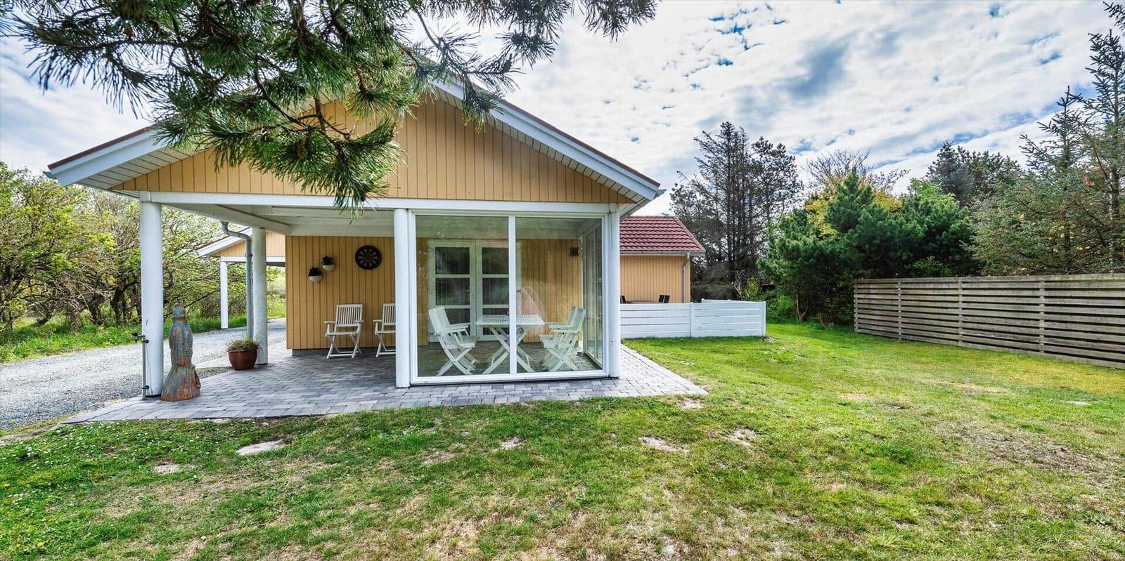 Haus mit überdachter Terrasse und Glasveranda. Weiße Möbel und grüner Garten.