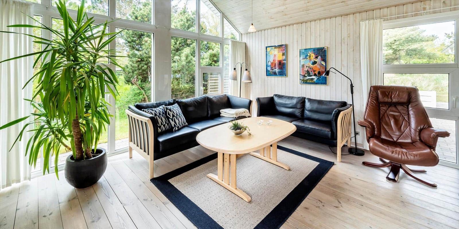 Wohnzimmer mit schwarzen Sofas, braunem Sessel und großem Fenster.