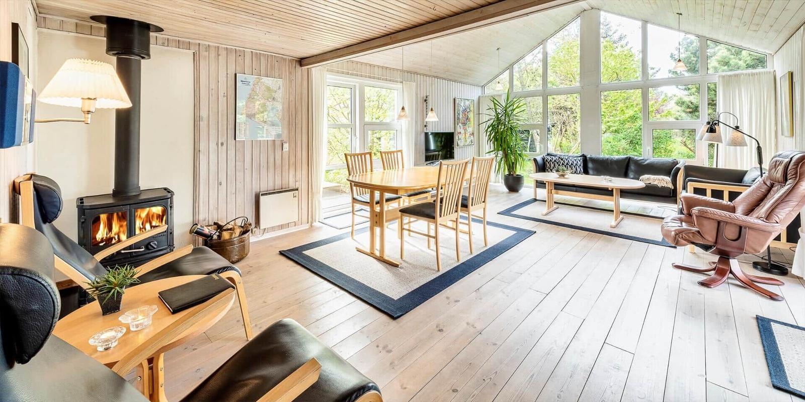 Wohnbereich mit Kamin, Esstisch und Sofa. Große Fenster, Holzboden und Möbel.