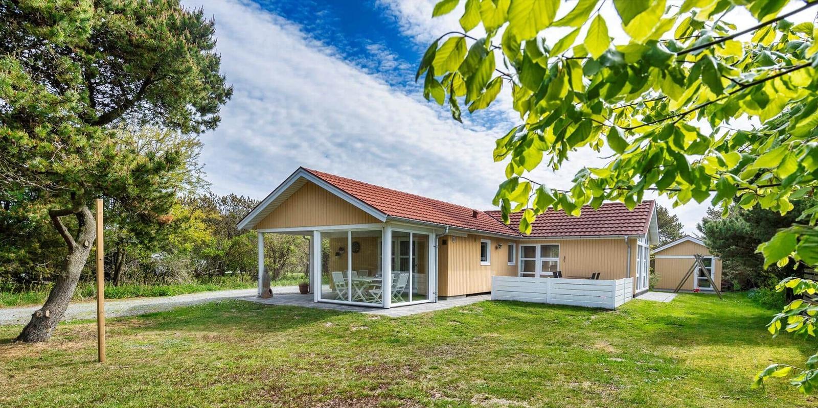Ein Haus mit Terrasse und Garten unter Bäumen. 