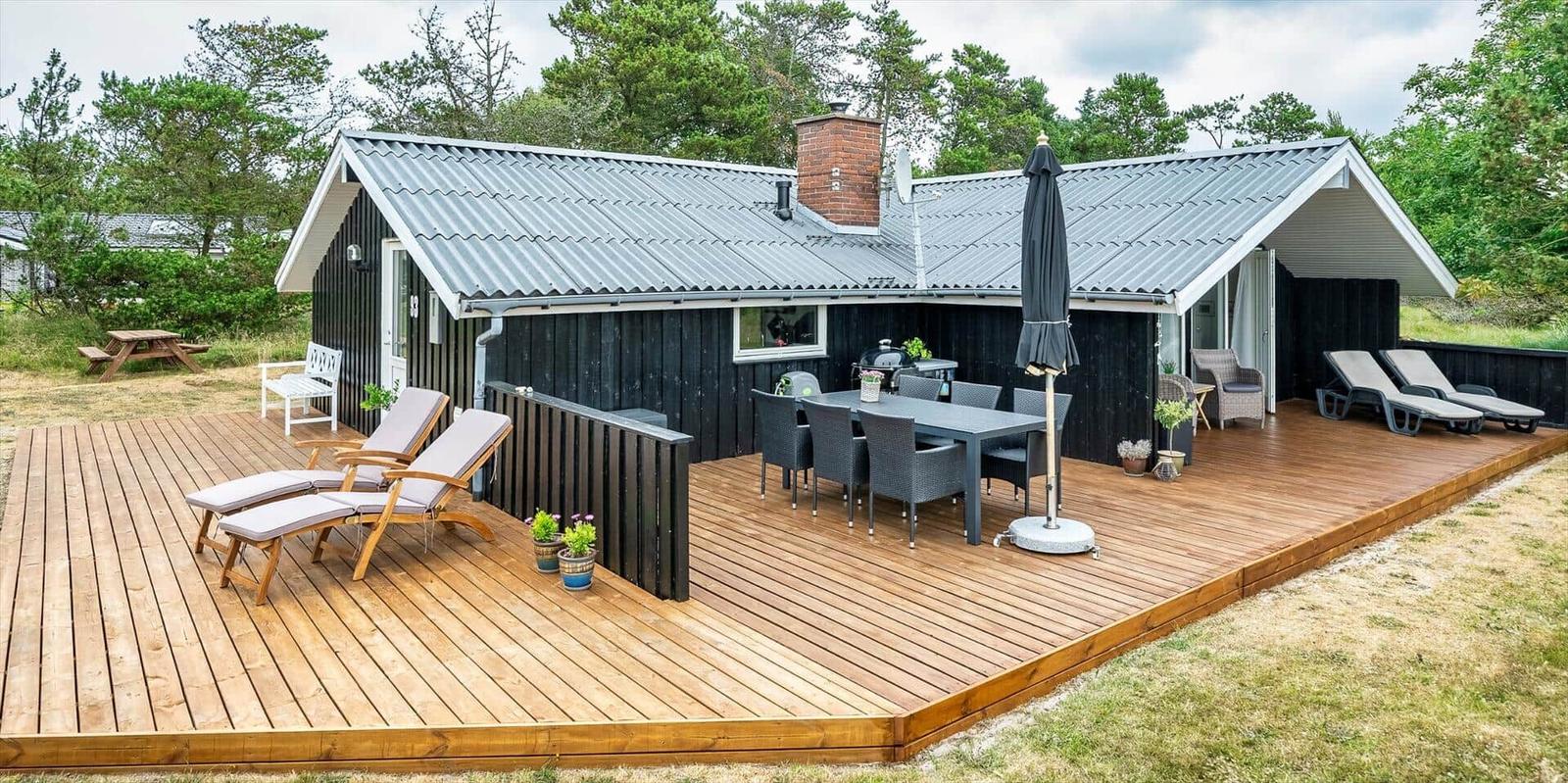 Haus mit großem Holzterrasse, Sitzgelegenheiten und Grillplatz.