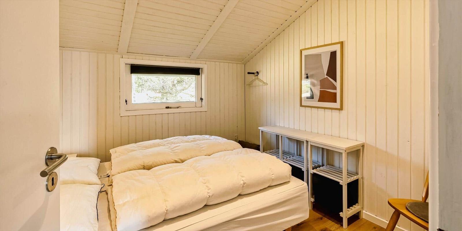 Schlafzimmer mit Bett, Fenster und Kleiderständer an der Wand.