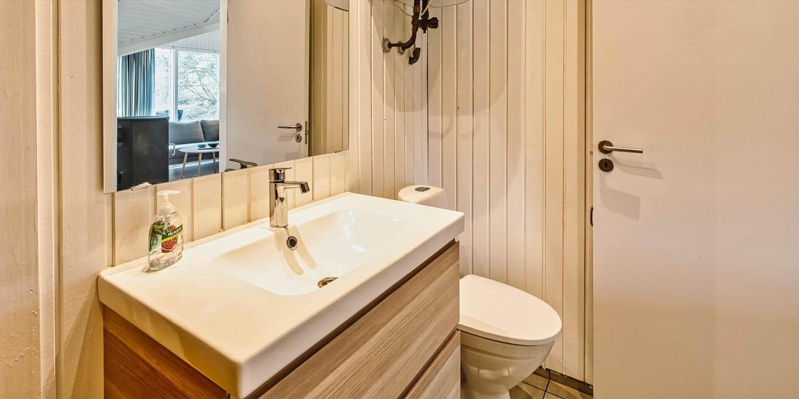 Badezimmer mit Waschbecken, Spiegel und Toilette. Holzfront und weiße Fliesen.
