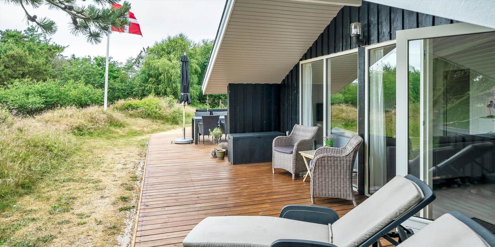 Terrasse mit Liegestühlen, Tisch und Stühlen. Daneben Flagge und Grünflächen.