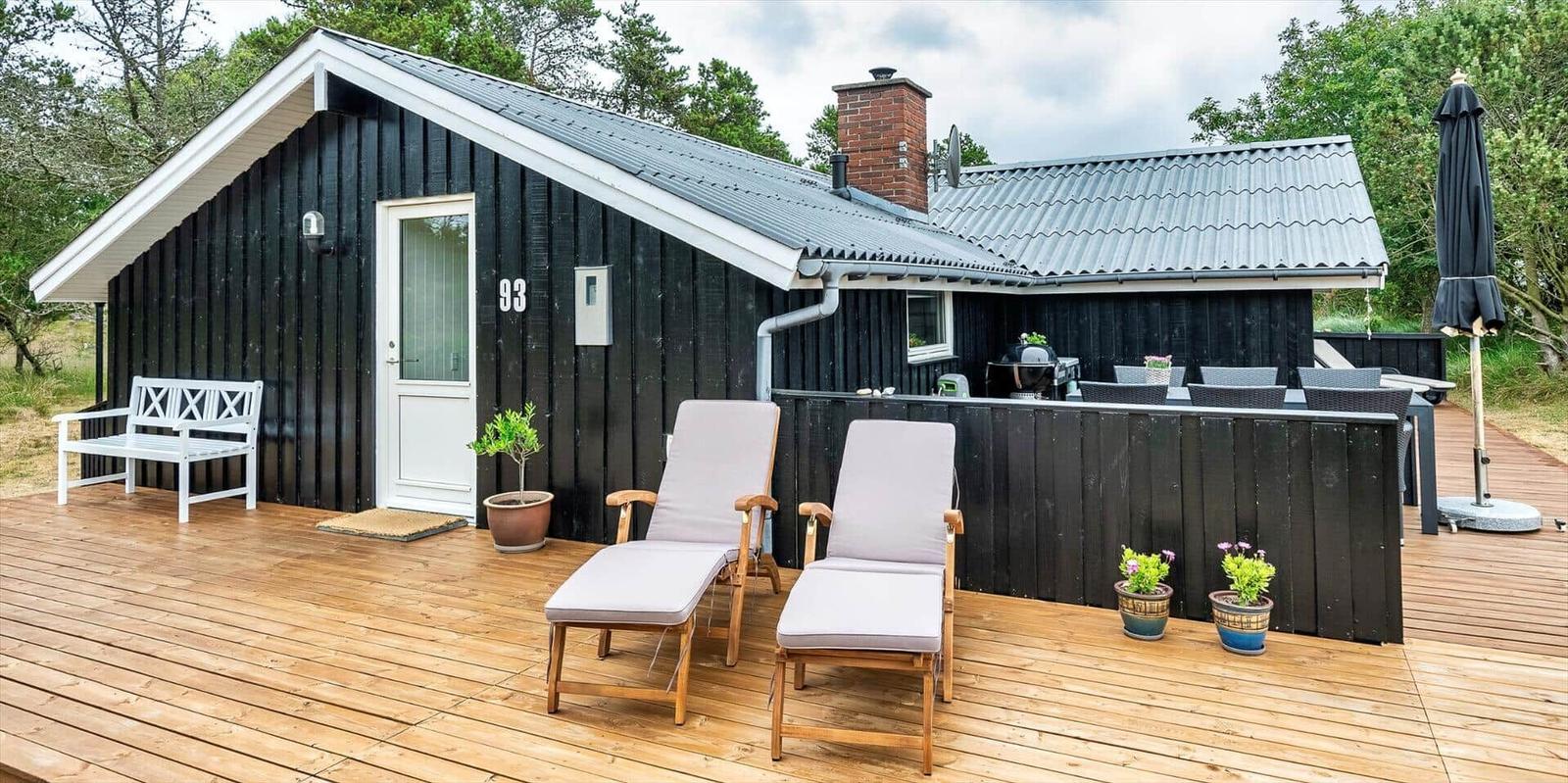Schwarzes Holzhaus mit Terrasse, Liegestühlen und Grillplatz.
