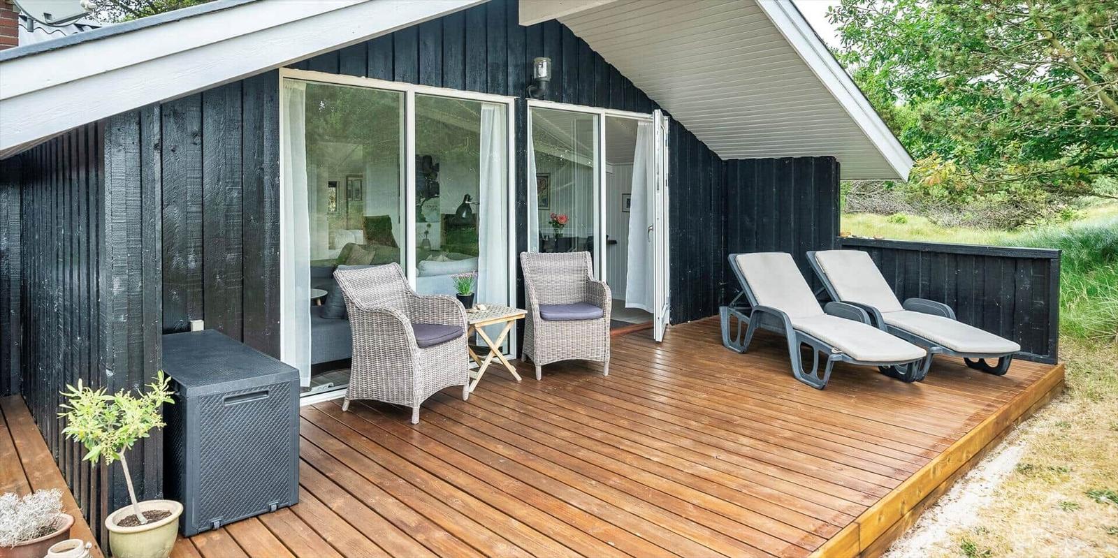 Terrasse mit Liegen und Sitzgelegenheiten vor einem Haus mit Schiebetüren.