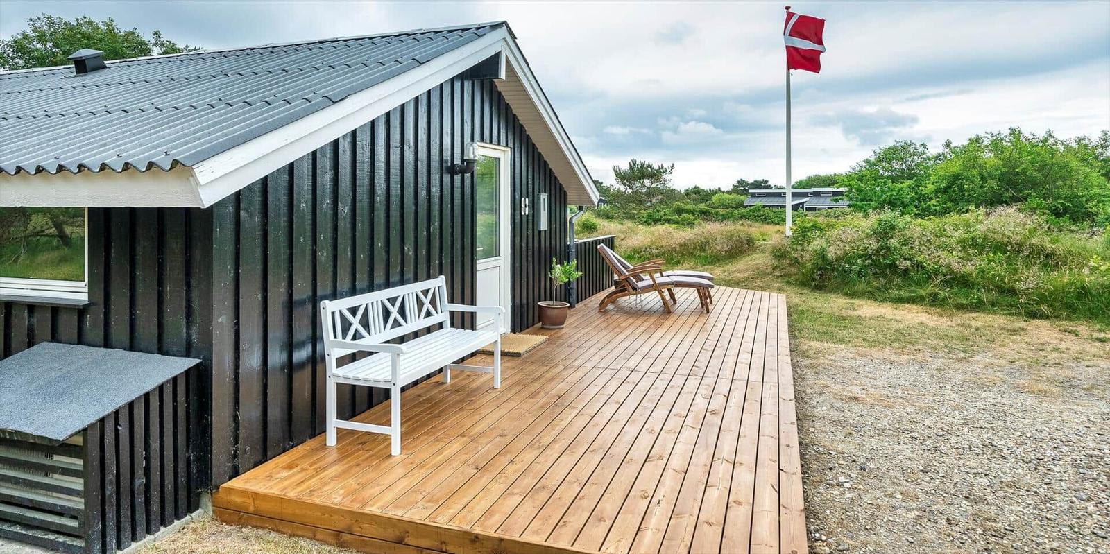 Hütte mit Holzterrasse, weißem Stuhl und Liegestühlen. Daneben weht die dänische Flagge.