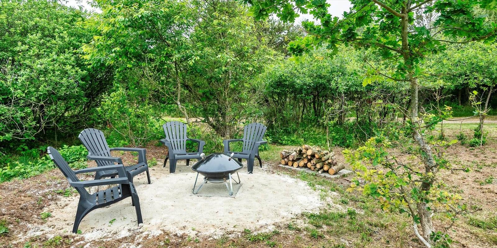 Außenbereich mit vier Sitzgelegenheiten und Grillplatz im Wald.