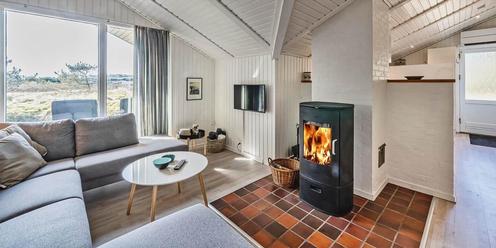 Wohnzimmer mit Kamin, Sofa und großem Fenster mit Blick auf die Landschaft.