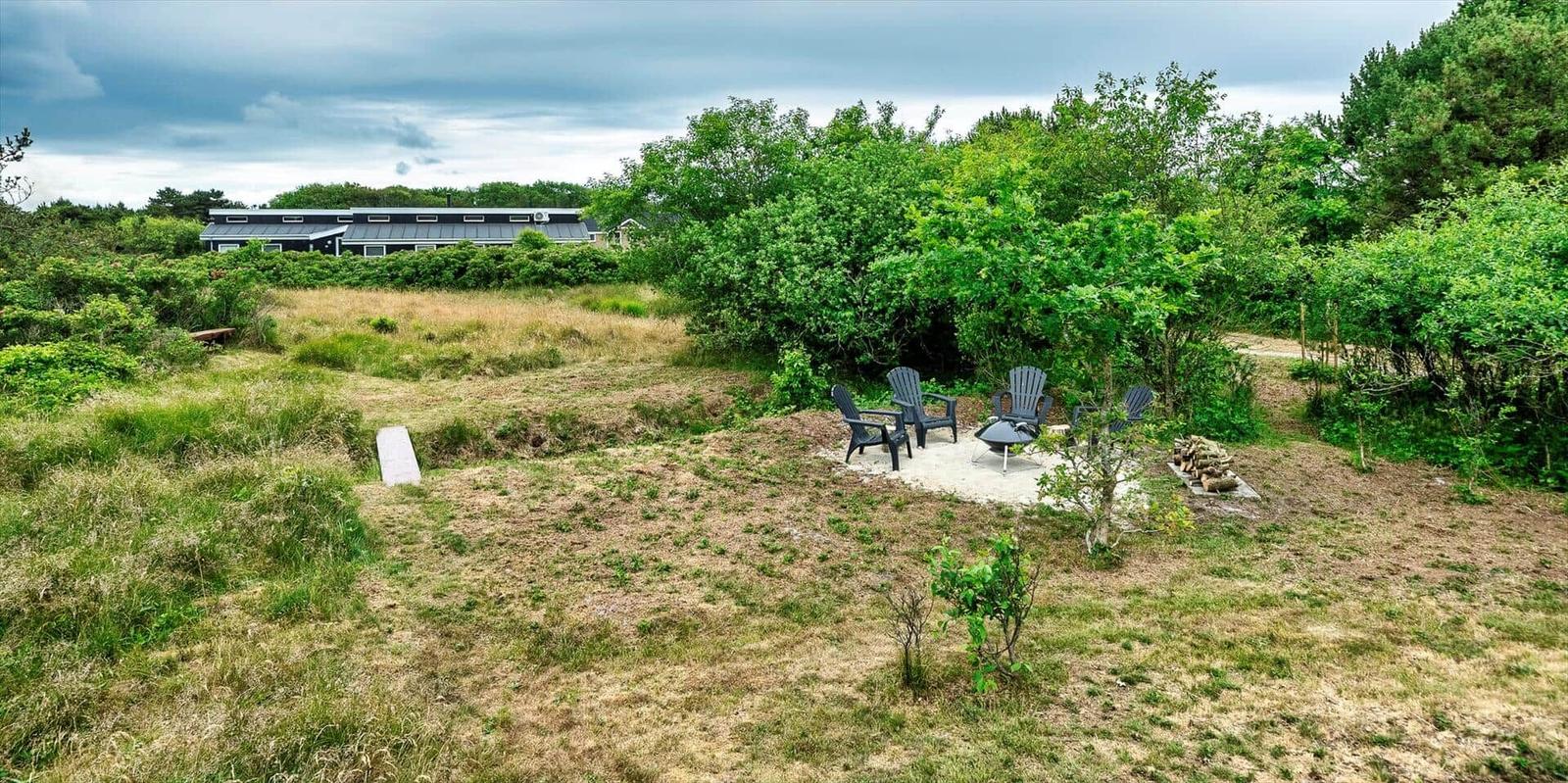 Terrasse mit Sitzgelegenheiten und Grillplatz im Grün. Im Hintergrund das Haus.