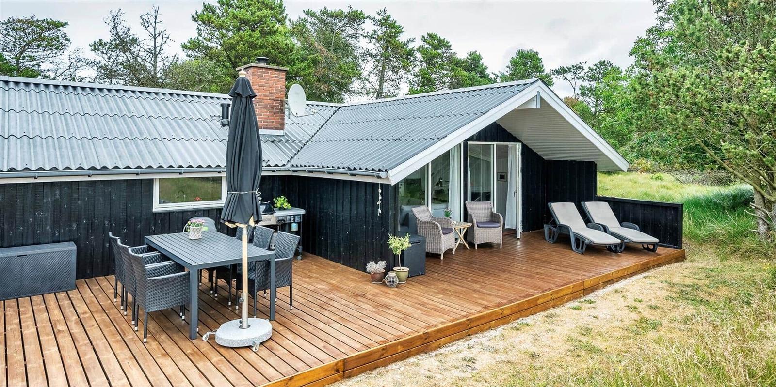 Terrasse mit Tisch, Stühlen und Liegen. Haus mit Holzverkleidung und Dach.