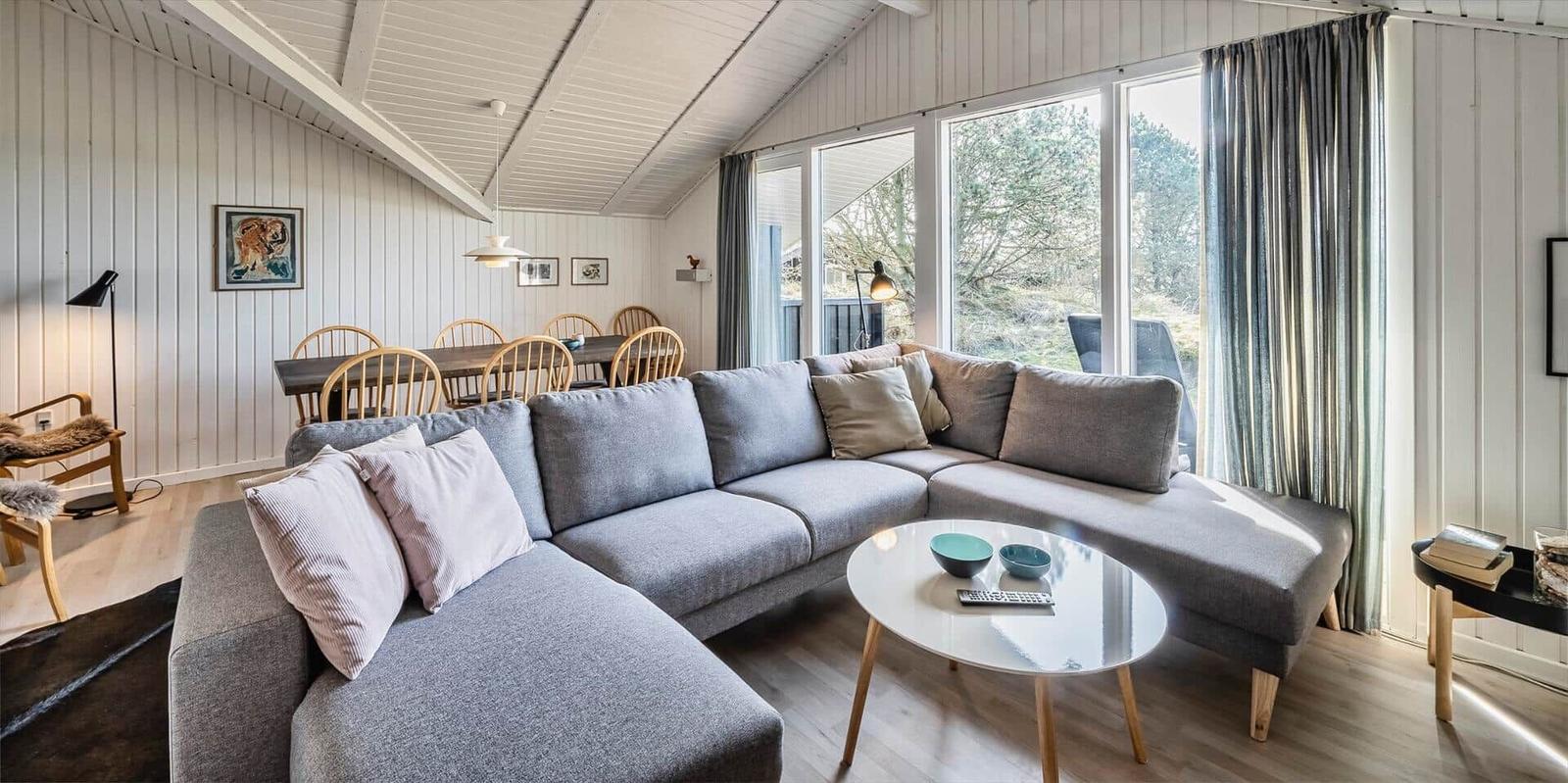 Ein Wohnzimmer mit grauem Sofa, runden Tisch und großen Fenstern.