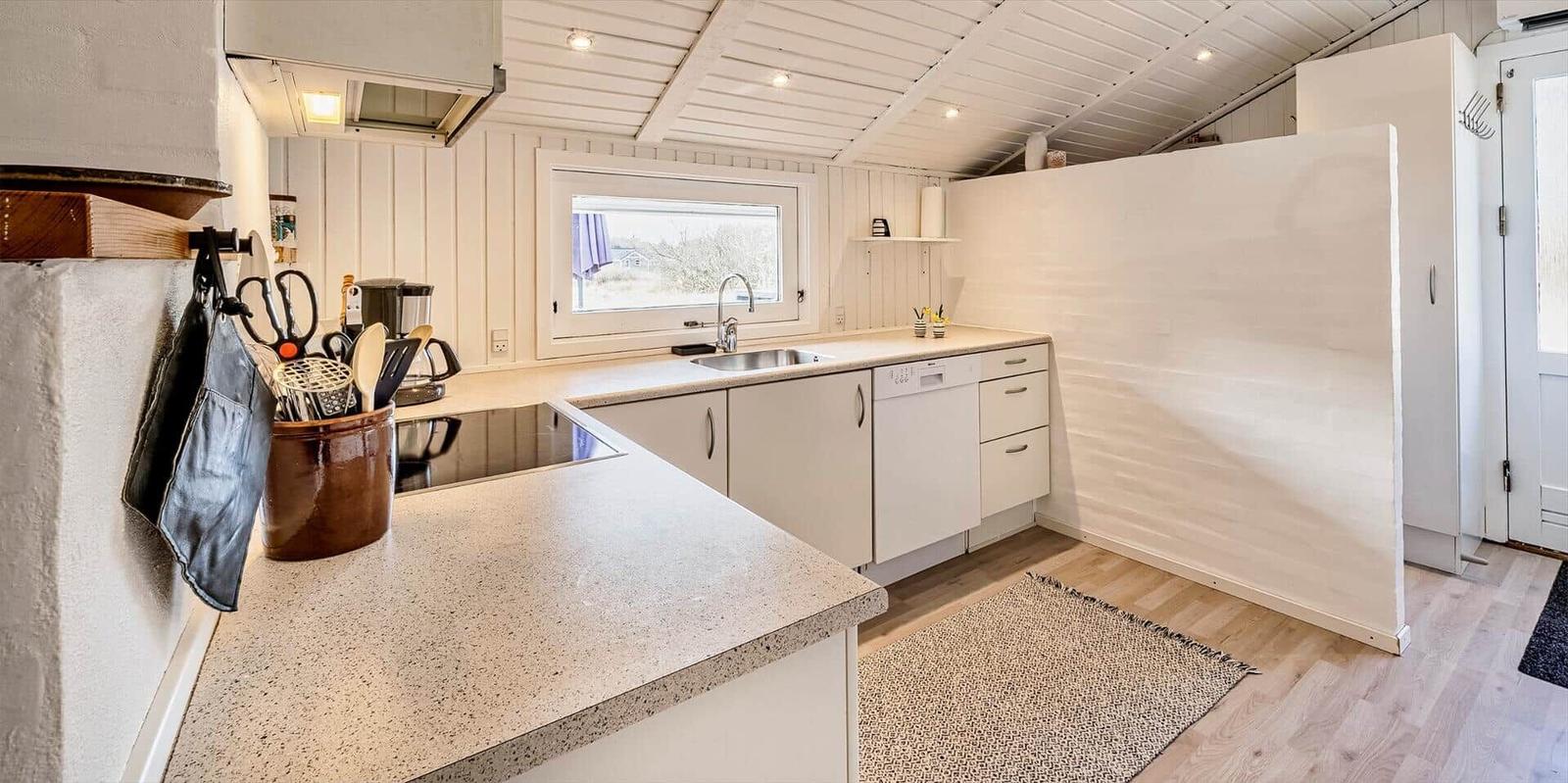 Küche mit Arbeitsplatte, Spüle und Waschmaschine. Fenster und Holzboden.