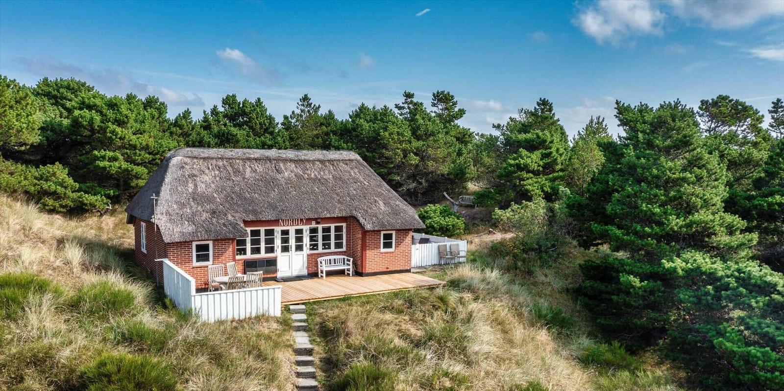 Rotes Holzhaus mit Strohdach, Terrasse und Garten im Wald.