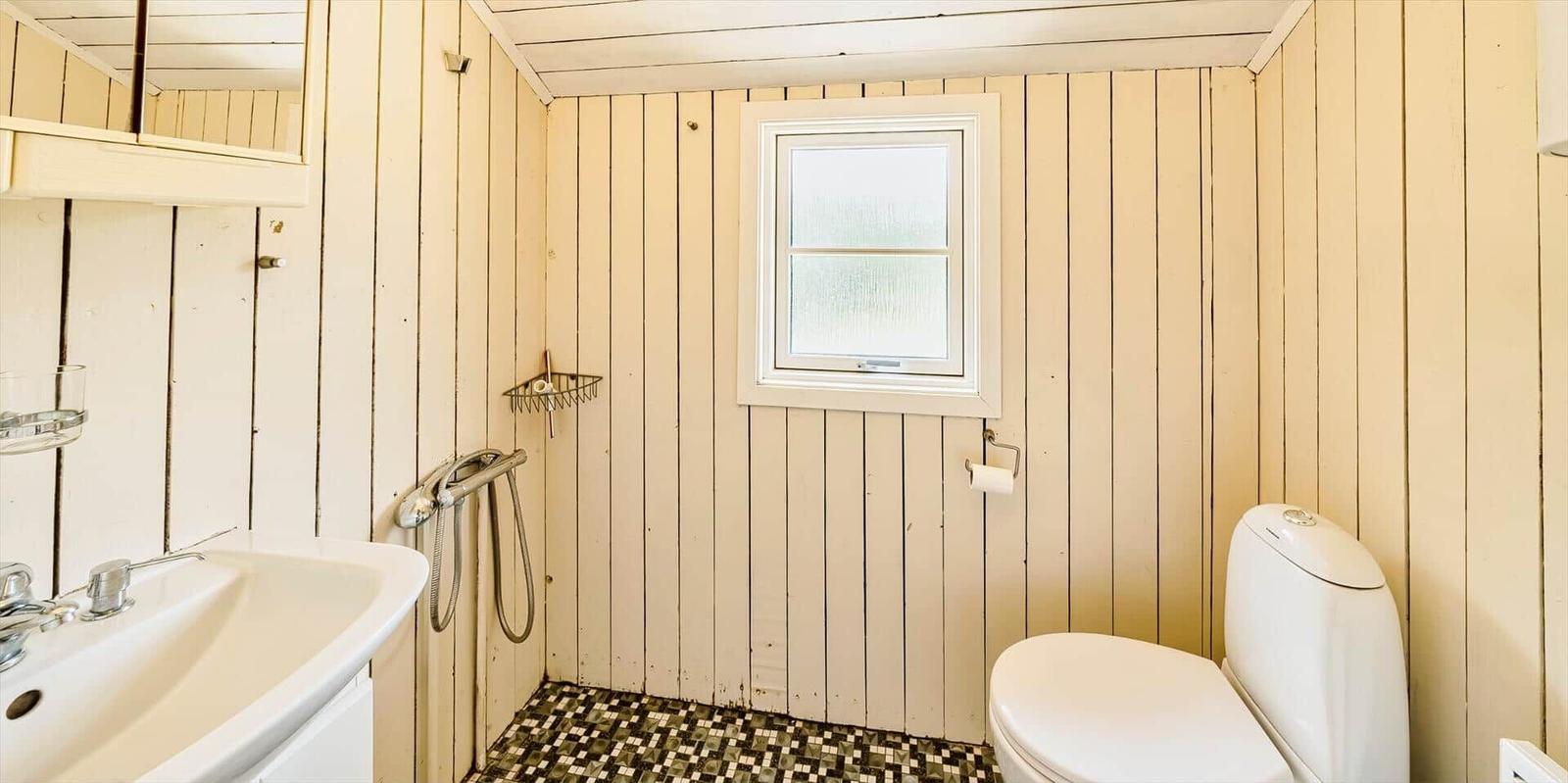 Badezimmer mit Toilette, Waschbecken und Dusche. Holzwände und Fliesenboden.