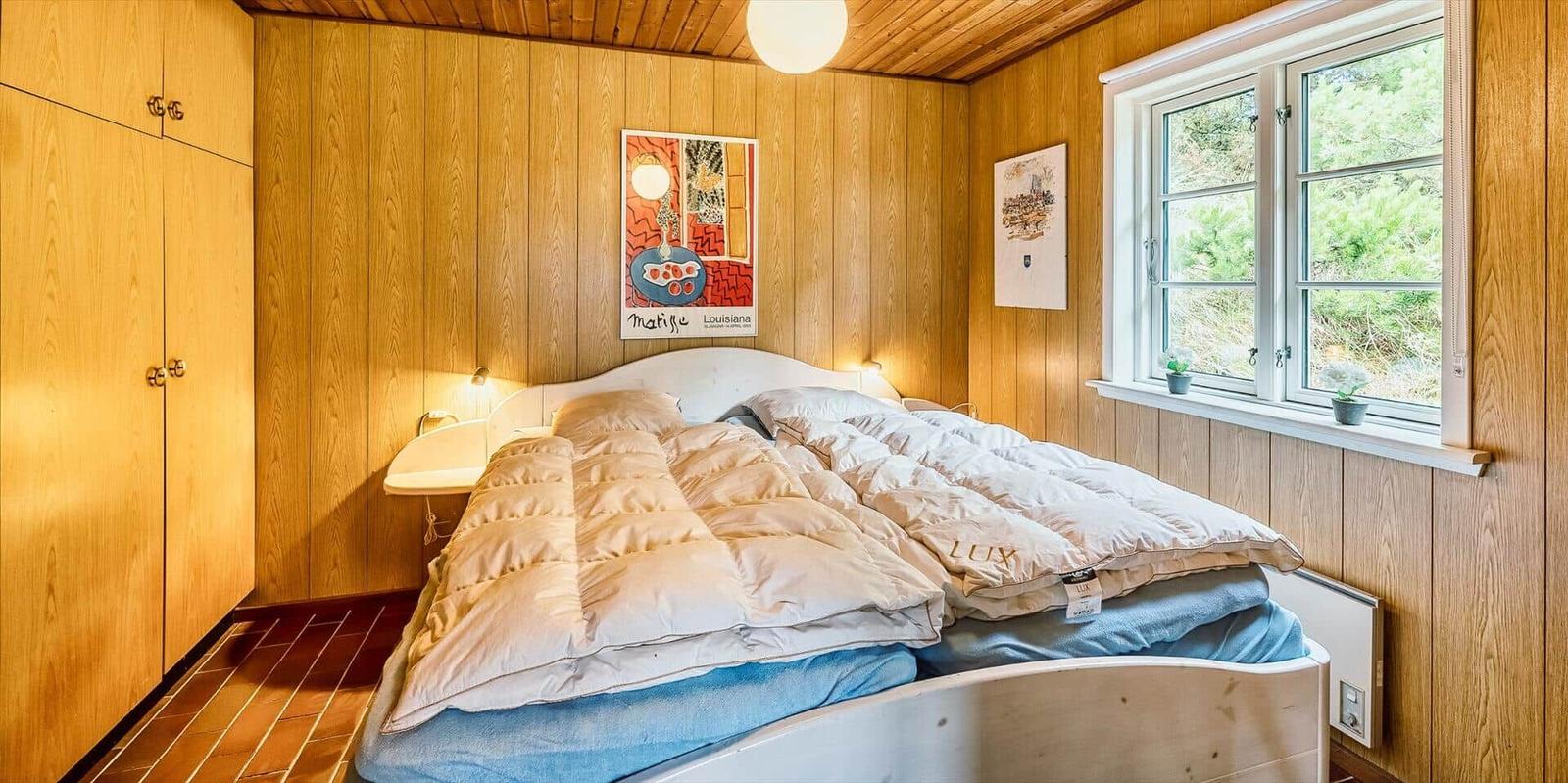 Schlafzimmer mit Holzwand, Bett und Fenster mit Blick auf Grün.