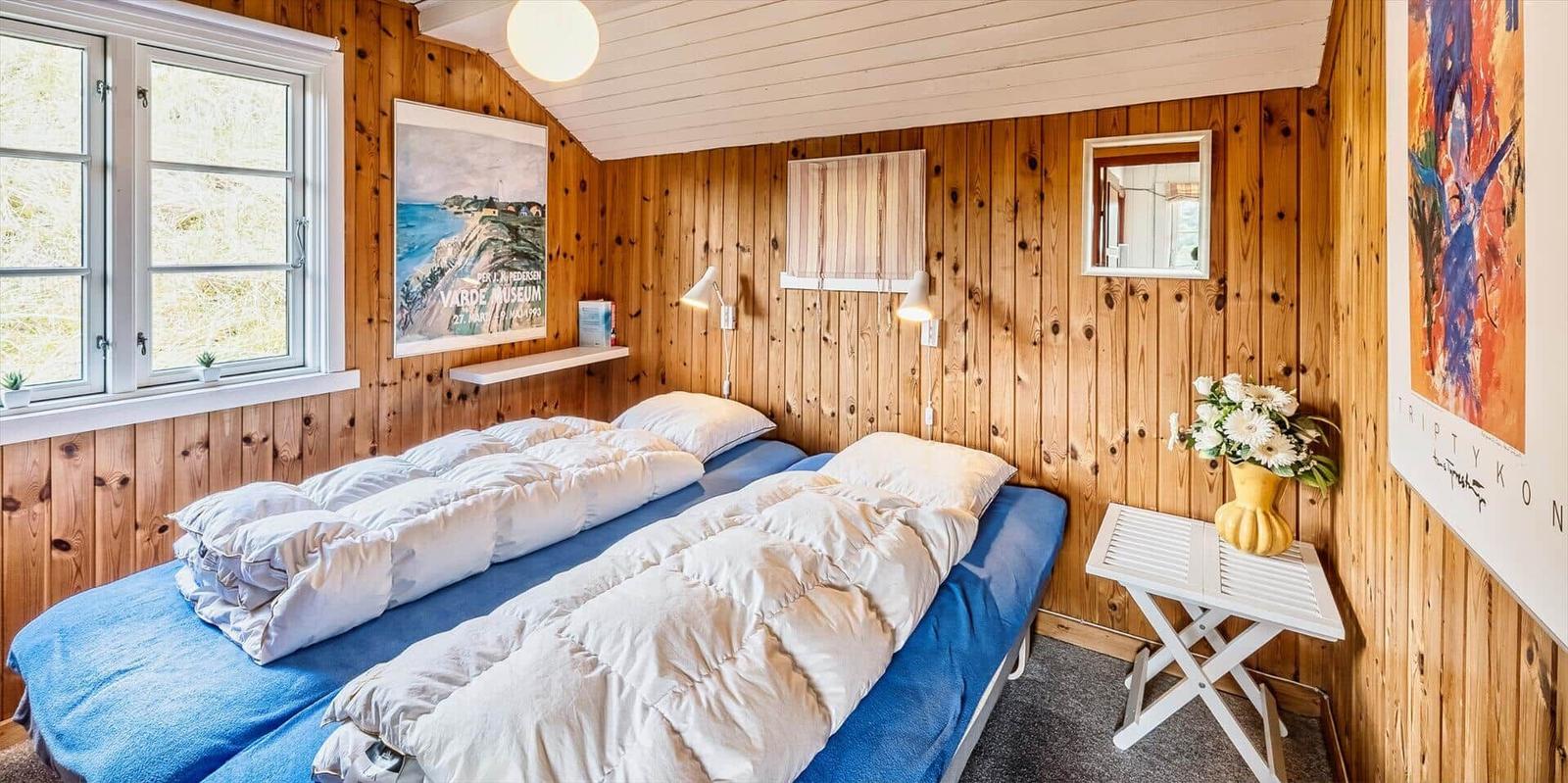 Zimmer mit zwei Betten, Holzwänden und Fenster. Tisch mit Blumen und Wandbilder.