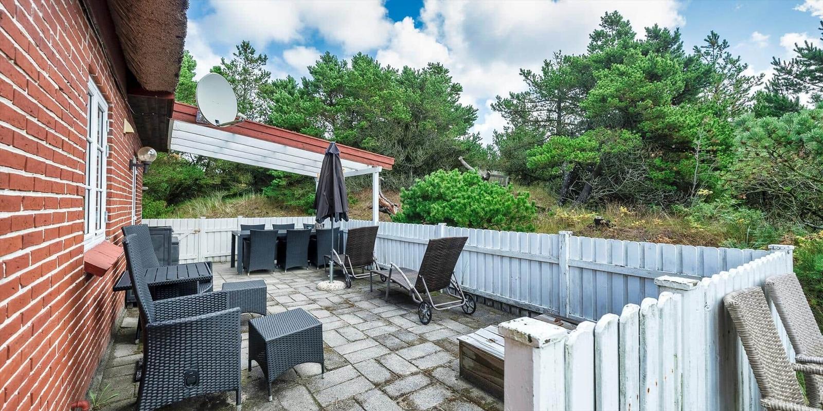 Terrasse mit Sitzgelegenheiten, Sonnenschirm und Blick auf grüne Bäume.