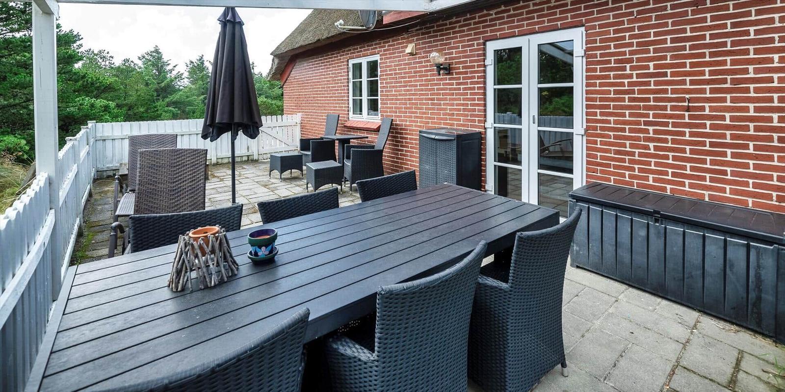 Terrasse mit Tisch, Stühlen und Sonnenschirm neben rotem Backsteinhaus.