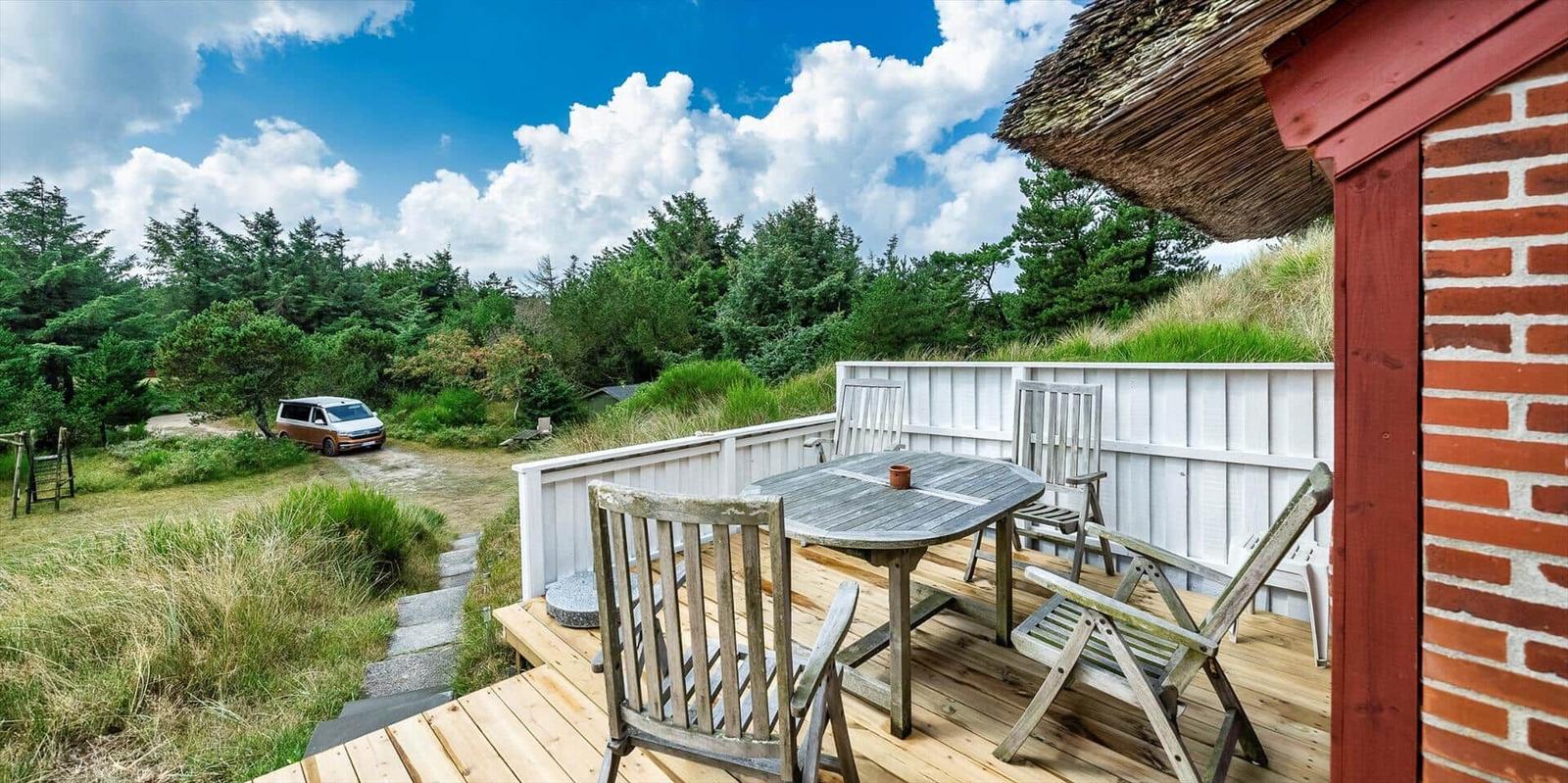 Terrasse mit Tisch und Stühlen neben einem Haus mit rotem Ziegel und strohgedecktem Dach.