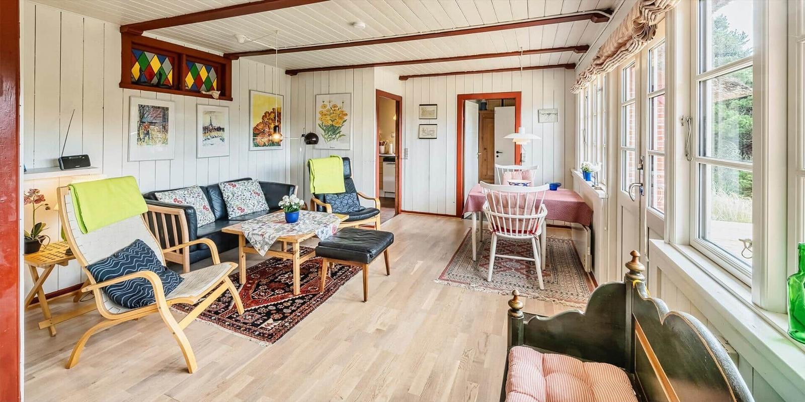 Wohnzimmer mit Sofa, Stühlen und Esstisch. Holzboden, Fenster und Wandbilder.