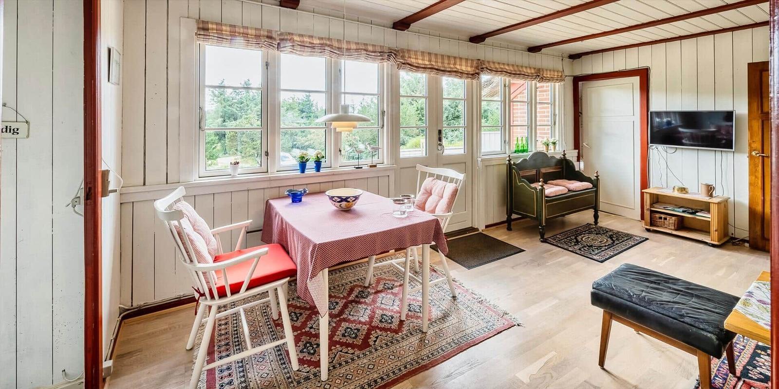 Essbereich mit Tisch, Stühlen und Fenstern. Wohnbereich mit Sofa und Fernseher.