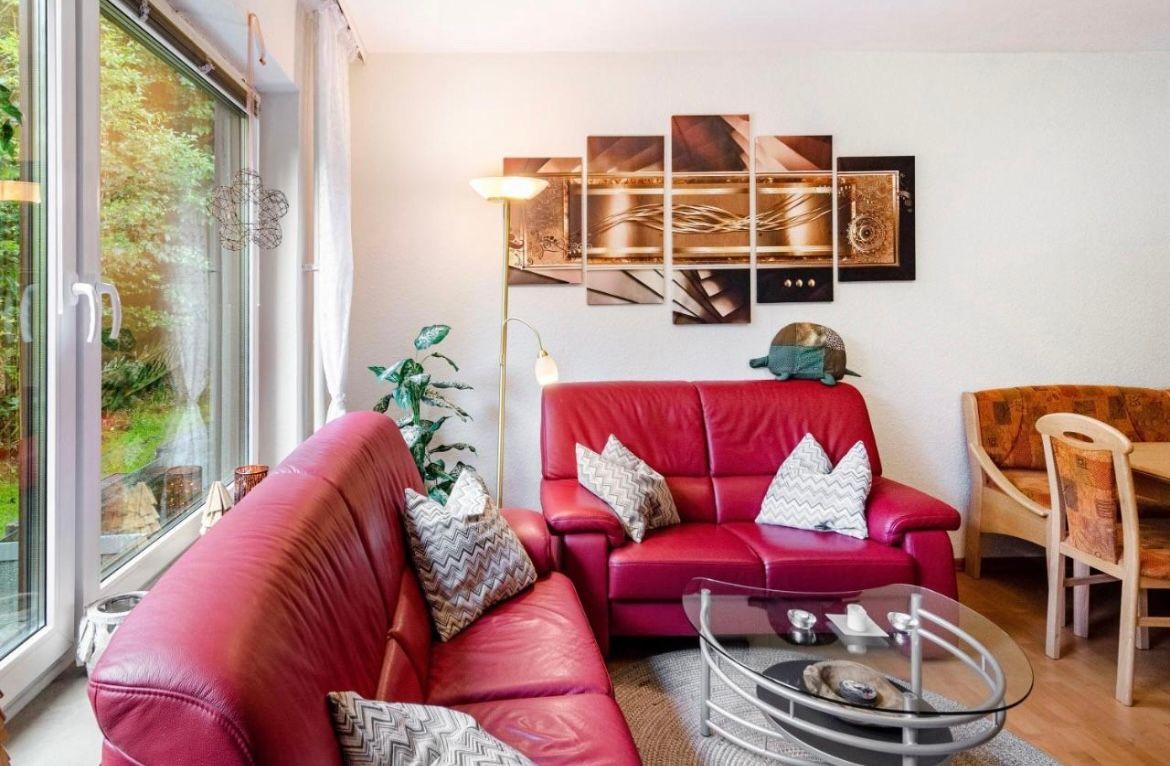 Ein Wohnzimmer mit rotem Ledersofa, Glas-Tisch und Wandbildern.