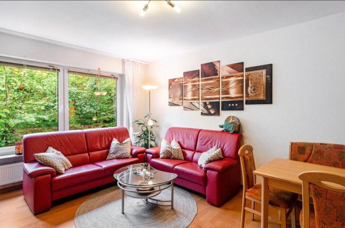 Wohnzimmer mit rotem Sofa, Glas-Tisch und Essplatz. Fenster mit Blick auf Wald.