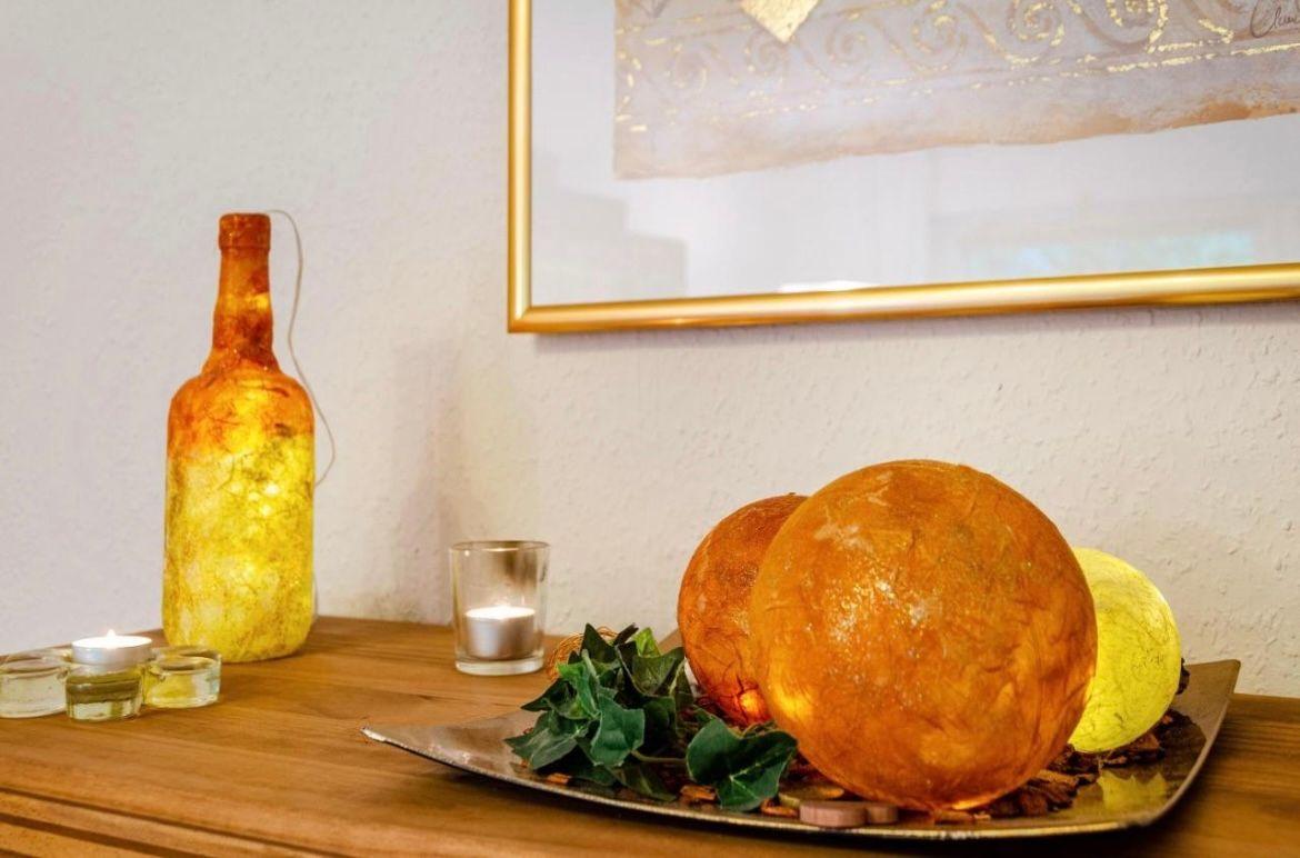 Holztisch mit dekorativen Kugeln, Kerzen und einer beleuchteten Flasche.