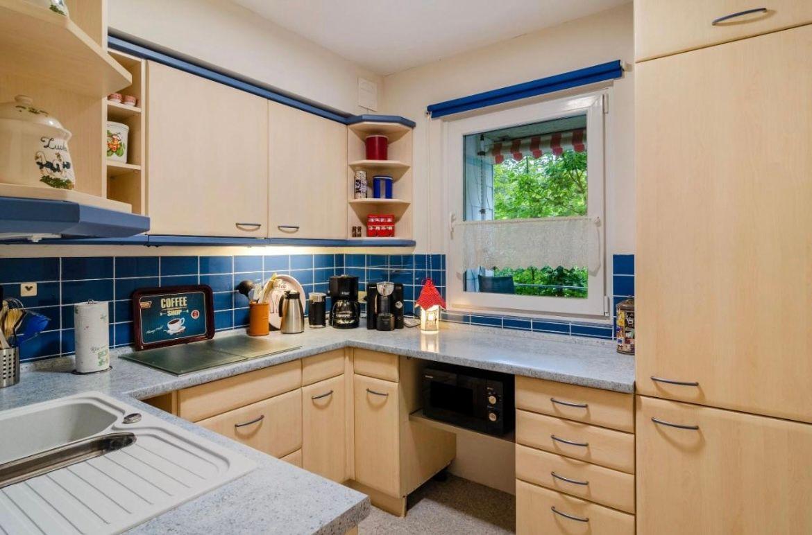 Küche mit hellen Schränken, blauer Fliesenwand und Fenster zum Garten.