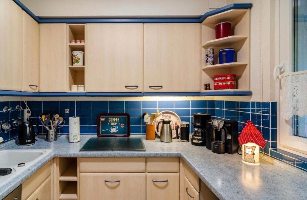 Küche mit Holzschränken, blauer Fliesenspiegel und Arbeitsplatte mit Küchengeräten.