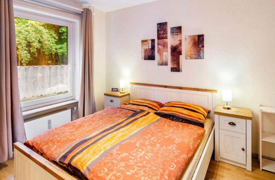 Schlafzimmer mit Bett, zwei Nachttischen und Fenster mit Blick auf Grün.