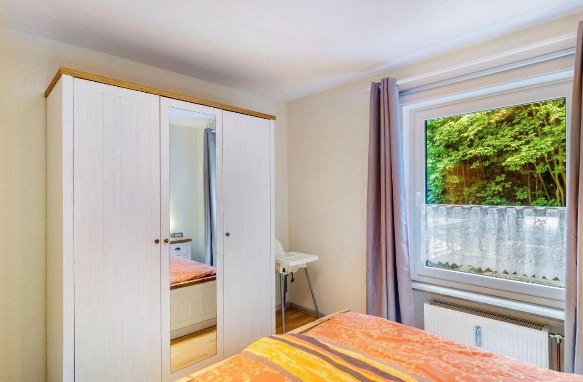 Schlafzimmer mit Doppelbett, Kleiderschrank und Fenster mit Blick auf Grün.