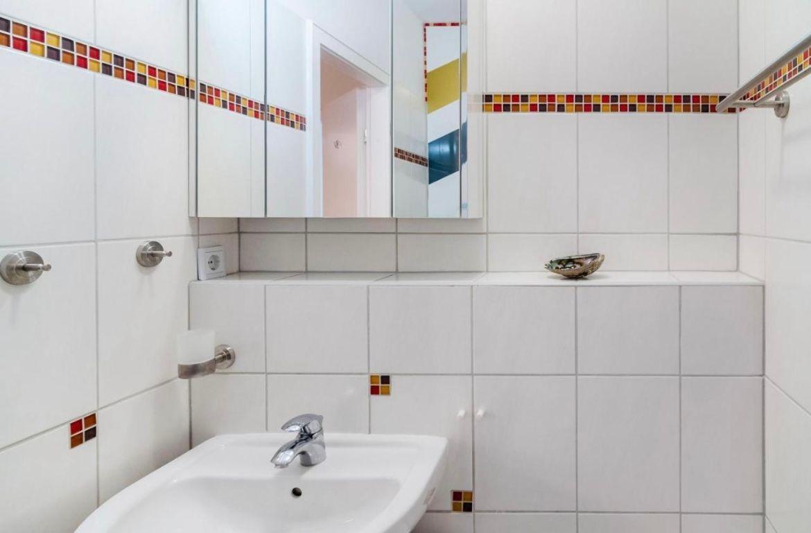 Badezimmer mit Waschbecken, Spiegelschrank und bunten Fliesenstreifen.