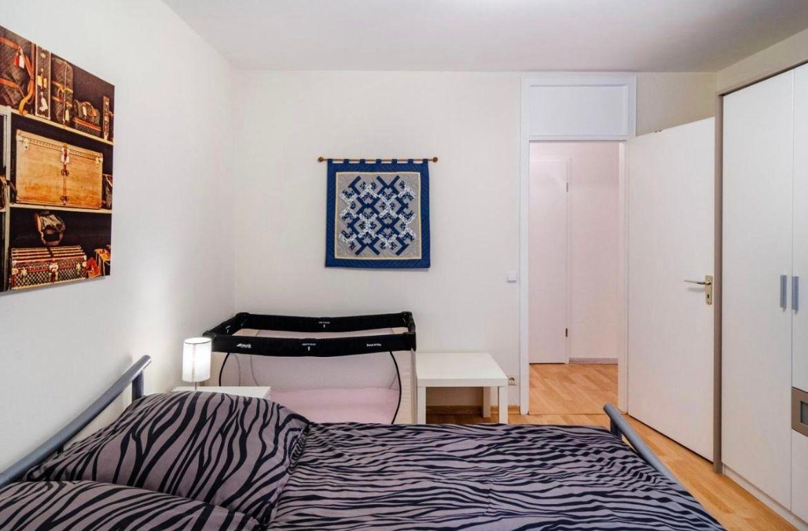 Schlafzimmer mit Bett, Wiege und Kleiderschrank. Wandbild und Holzboden sichtbar.