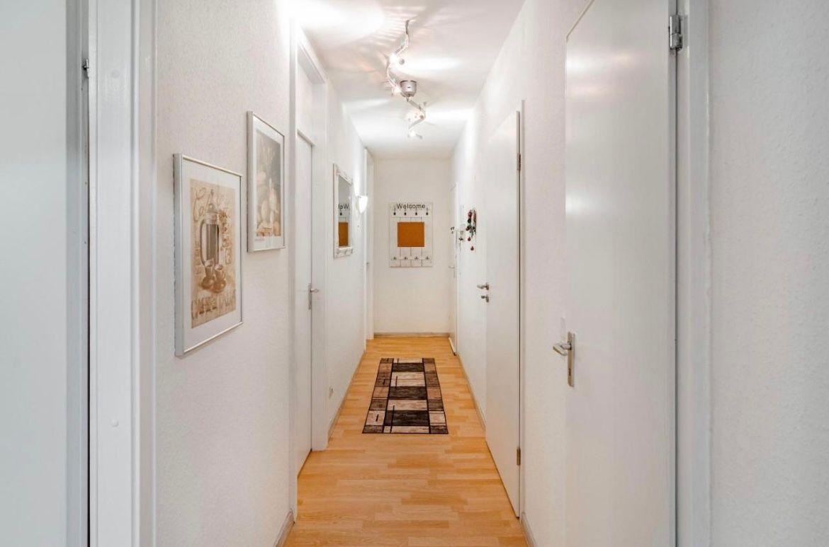 Flur mit Holzboden, Tapete und Bildern an den Wänden. Teppich und Tür sind sichtbar.