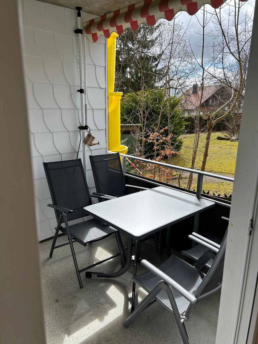 Balkon mit Tisch und Stühlen, rotem Sonnenschutz und Blick auf Grünflächen.